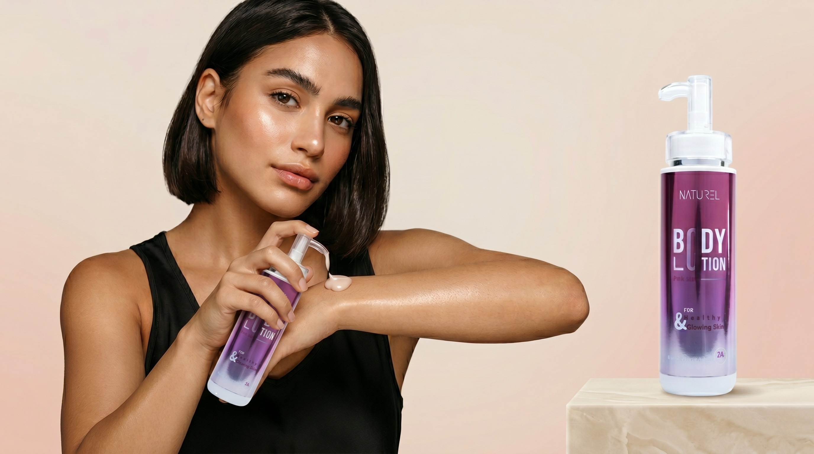 Woman applying purple body lotion to her arm with a bottle of the same product displayed next to her on a beige background.